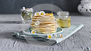 Many small pancakes with honey or syrup. Delicious traditional breakfast. Spring flowers as food styling in photography. Gray