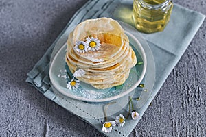 Many small pancakes with honey or syrup. Delicious traditional breakfast. Spring flowers as food styling in photography. Gray