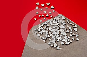 Many small wooden hearts of different sizes fly out of empty kraft envelope on clean red background. Visual content for the