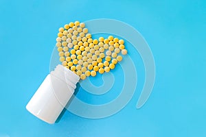 Many small yellow pills spilled out of a white jar on a blue background in the shape of a heart