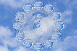 Many soap bubbles form a clock showing five minutes to twelve o`clock against blue sky