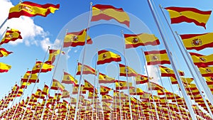 Many Spain Flags on flagpoles against blue sky.