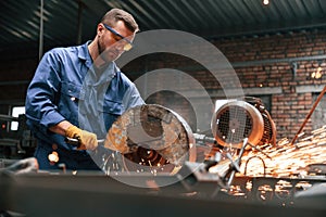 Many of the sparks. Welding the metal. Factory worker in blue uniform is indoors