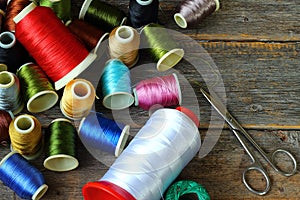 Spools of multicolored threads and scissors lying on wooden background