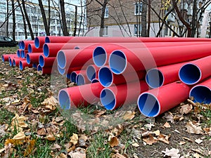 Many stacked red and blue pvc plastic plumbing tubes pipes lying on the ground outdoors