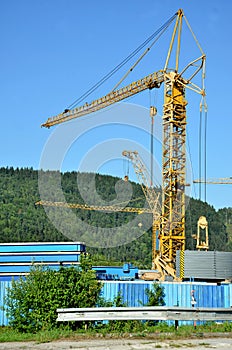 Many standing yellow tower cranes, forested hill and blue sky in background