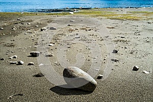 Many stones with different sizes on the beach in sunshine with seagrass and blue sea in the background in summer season