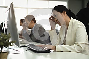 Many stress of asian employee with business suit in front of their monitor, keyboard next to mouse and house phone in customer
