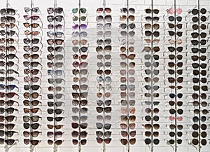 Many sunglasses in eyewear store, display on white wall