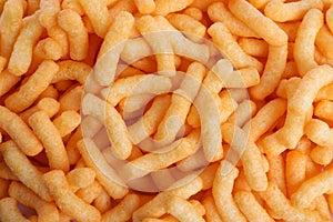 Many tasty cheesy corn puffs as background, top view