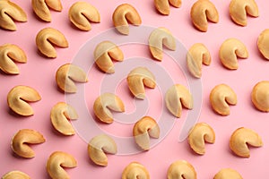 Many tasty fortune cookies with predictions on pink background, flat lay