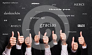 Many thumbs up with the word `thank you` in many languages in front of a blackboard