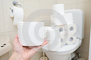 Many toilet paper rolls at home of hoarder, buying too much of hygienic means during pandemia, a hand holding a roll of