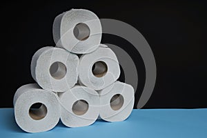 Many toilet paper rolls stacked in pyramid shape. Soft hygienic paper. Wooden table on black background