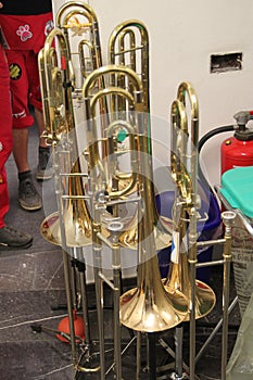 Many trombones stand around on their trombone stands in the aisle. Imperial College London big band rehearsal room. Brass