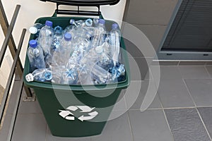 Many used plastic bottles in trash bin near entrance outdoors. Recycling problem