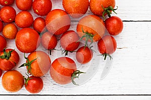 Many wet red tomatoes with stalks on white wood board from abov