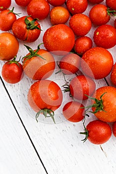 Many wet red tomatoes with stalks on white wood board from abov