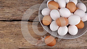 White and brown eggs in plate and one egg next to a small feather on an old wooden desk, place for text