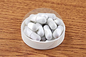 Many white capsules in plastic cap on wooden background