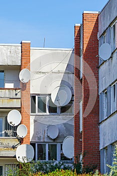 Many white parabolic satellite antenna dishes hanged on wall of suburban perfab block of flats