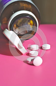 Many white pill tablets drop from the bottle on the pink floor