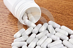 Many white pills and plastic vial on wooden background