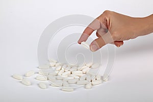 Many White pills scattered with hand holding a pill