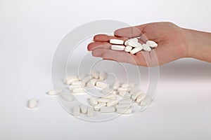Many White pills scattered with hand holding pills