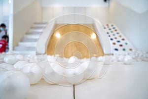 Many of white plastic balls in the children`s playroom in front of blur Wooden slide flanked by stair and colorful strength rock