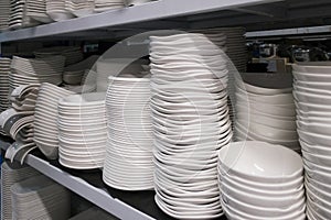 Many of white plate and bowl on shelves in kitchenware shop.