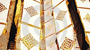 Many white ribbons with gold ornaments flutter in the wind in a Buddhist temple in Southeast Asia. Buddhist symbols Tung