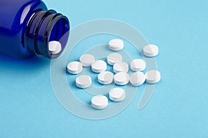 Many white tablets spilling out of package, Close up pills spilling out of pill bottle on blue background. Medicine, medical