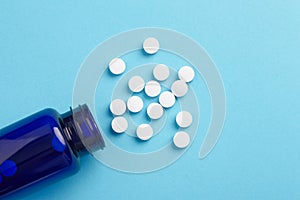 Many white tablets spilling out of package, Close up pills spilling out of pill bottle on blue background. Medicine, medical