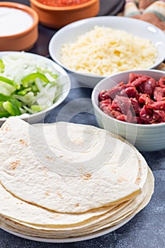 Many whole wheat flour tortillas and ingredients for tacos, fajitas or quesadilla, vertical