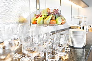Many wineglasses. Breakfast in restaurant of hotel. Plate with fruits and berries on a smorgasbord in the background. Bar