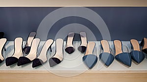 Many women`s shoes on wooden shelf for sale with gray or grey wall background.