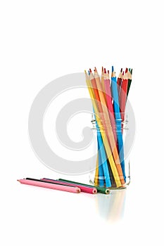 Many wooden colored crayons stand in a glass, isolated on a white background with reflection on the table top