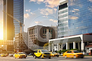 Many yellow taxis of different types drive quickly along the road in the city against the backdrop of skyscrapers