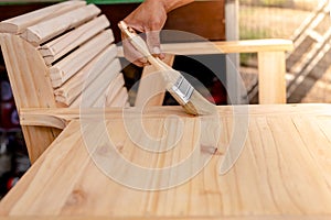 Manâ€™s hand holding a brush applying varnish paint on a wooden