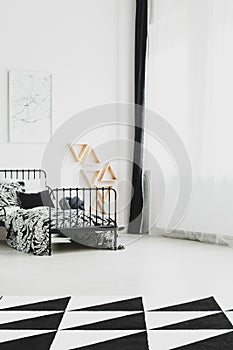 Map above industrial metal bed with black and white bedding and patterned rug on the floor