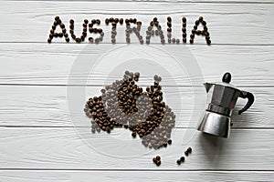 Map of the Australia made of roasted coffee beans laying on white wooden textured background with coffee maker