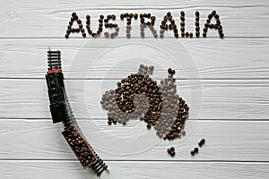 Map of the Australia made of roasted coffee beans laying on white wooden textured background with toy train