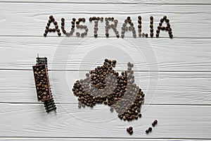 Map of the Australia made of roasted coffee beans laying on white wooden textured background with toy train