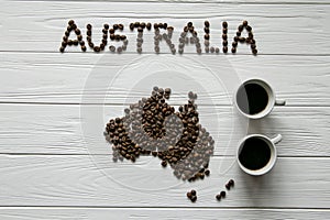 Map of the Australia made of roasted coffee beans laying on white wooden textured background with two coffee cups