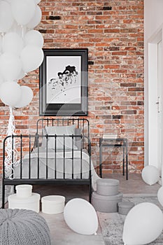 Map in black frame on brick wall in classy bedroom interior with industrial single bed with grey bedding and bunch of white