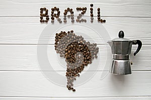 Map of the Brazil made of roasted coffee beans laying on white wooden textured background with coffee maker