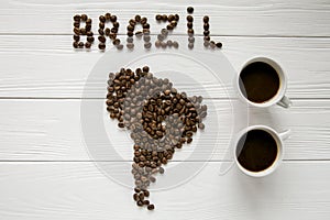 Map of the Brazil made of roasted coffee beans laying on white wooden textured background two cups of coffee