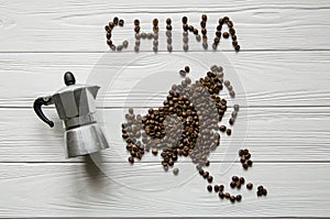 Map of the China made of roasted coffee beans laying on white wooden textured background with coffee maker