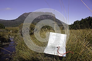 A map and a compass on a buttongrass plain in front of a rocky escarpment on Tasmania Australia`s Overland Track